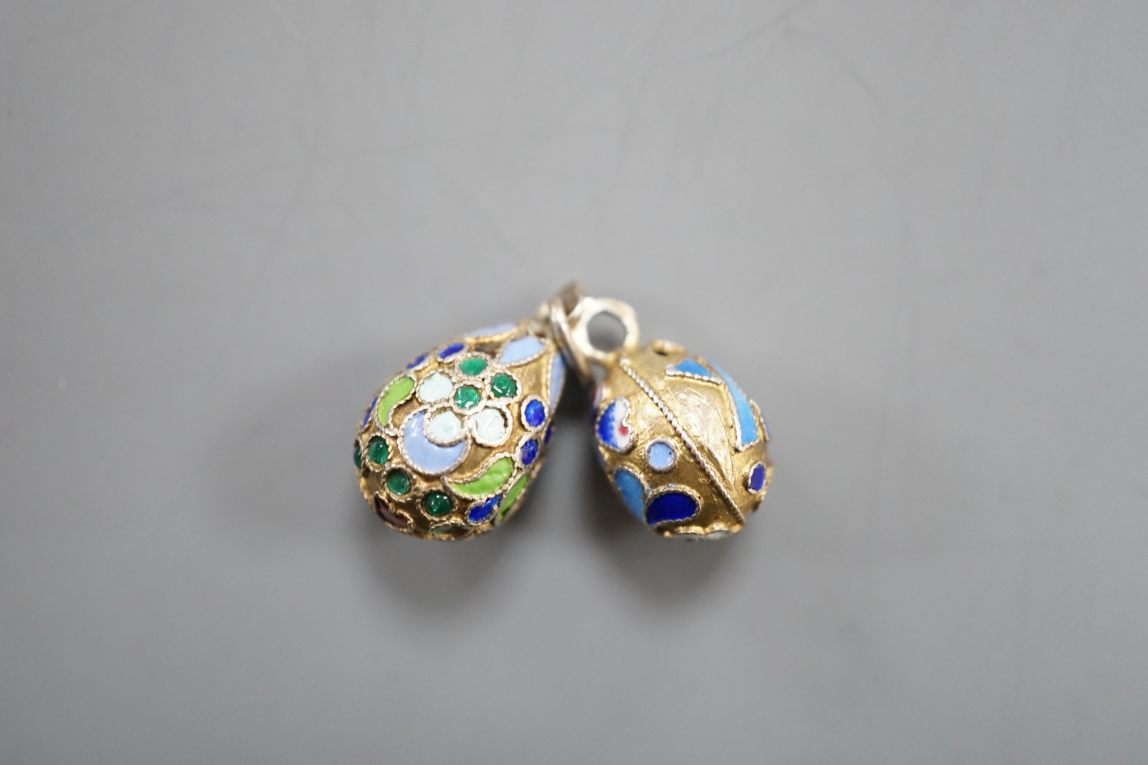 An early 20th century Russian 84 zolotnik and polychrome cloisonné enamel set egg pendant, maker's mark HT?, 17mm and a similar smaller egg pendant, maker's mark HM?.